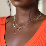 Woman wearing an orange top and layered necklaces against a neutral background
