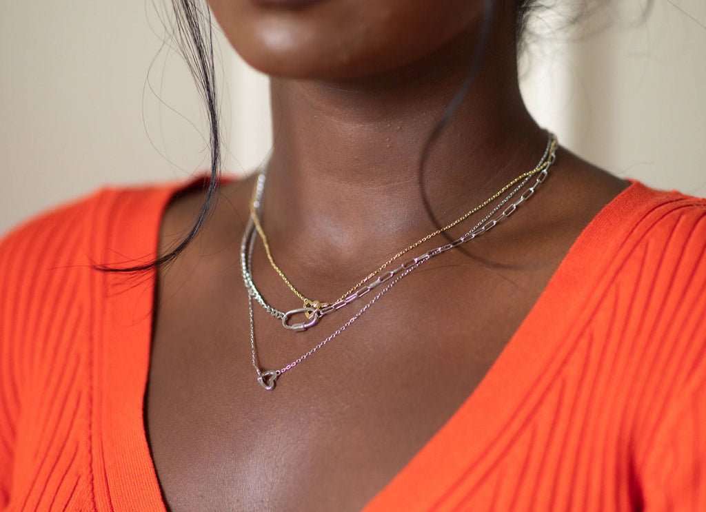 Woman wearing an orange top and layered necklaces against a neutral background